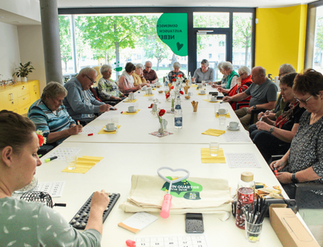An einem großen Tisch im Quartierszentrum in deer Brest-Straße 2 spielen ca. 20 Senioren hochkonzentriert Bingo.