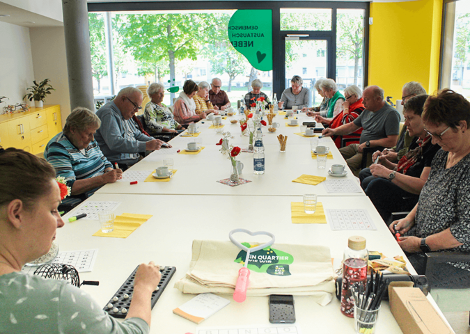An einem großen Tisch im Quartierszentrum  in deer Brest-Straße 2 spielen ca. 20 Senioren hochkonzentriert Bingo.